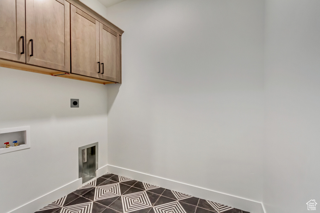 Washroom featuring dark tile patterned floors, washer hookup, baseboards, hookup for an electric dryer, and cabinet space
