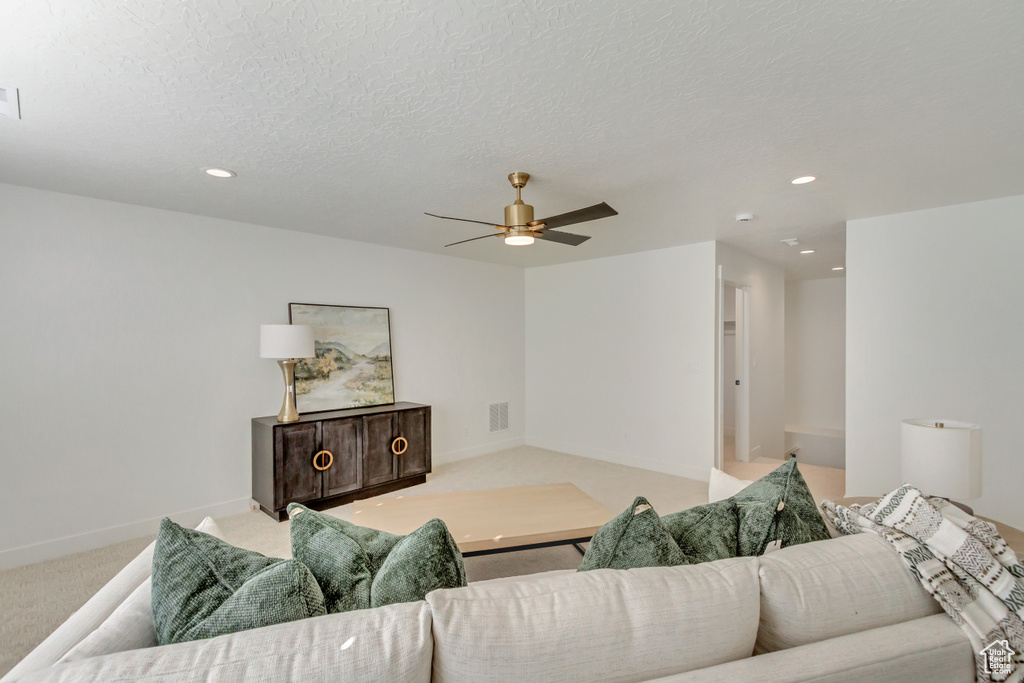 Living room with light colored carpet, ceiling fan, baseboards, and a textured ceiling