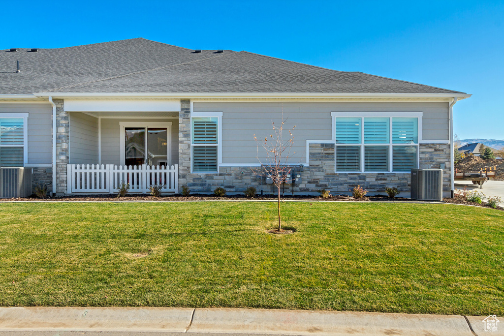View of front facade featuring stone siding, central AC, and a front lawn