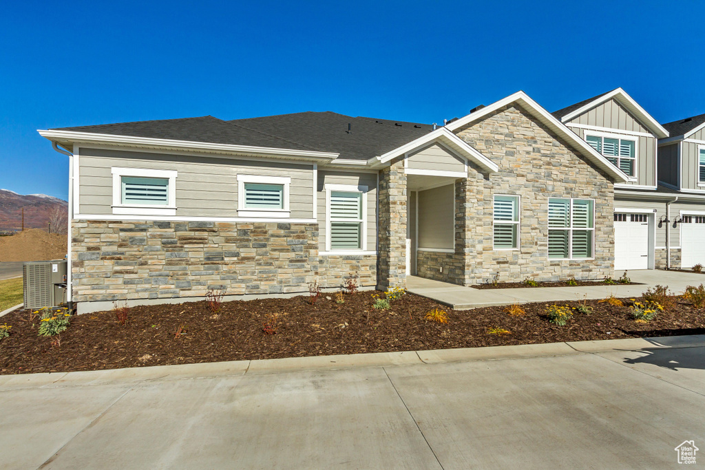 View of front of house featuring stone siding, concrete driveway, board and batten siding, central AC unit, and a garage