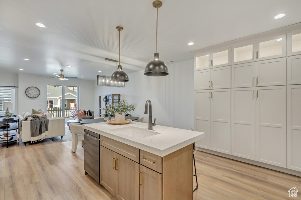 Kitchen featuring pendant lighting, a kitchen island with sink, a sink, and light wood-type flooring