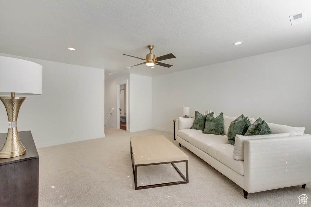 Living room featuring a ceiling fan, a textured ceiling, baseboards, light colored carpet, and visible vents