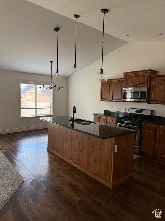Kitchen featuring a sink, appliances with stainless steel finishes, dark wood-style floors, a kitchen island with sink, and dark countertops