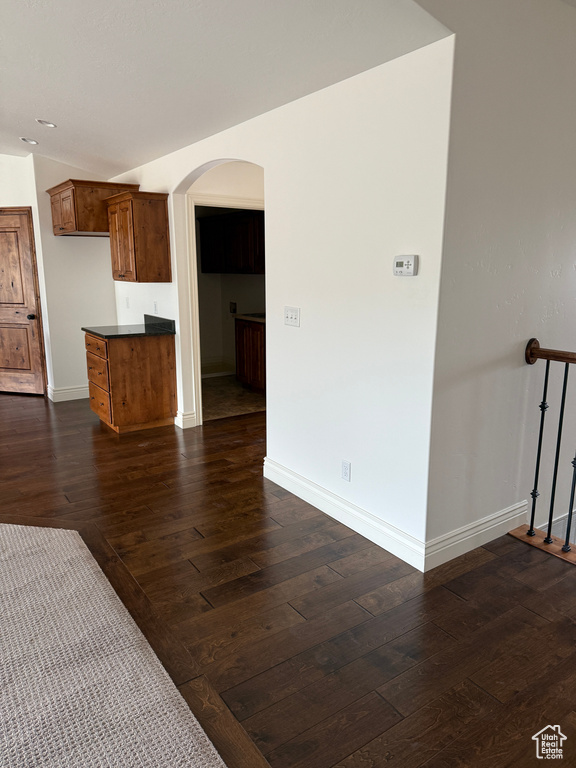 Interior space featuring arched walkways, dark wood-style floors, baseboards, and vaulted ceiling