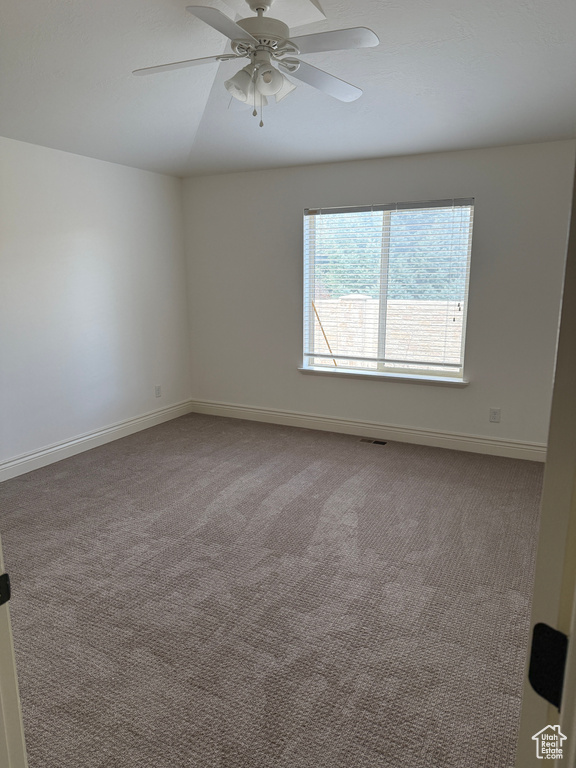 Carpeted empty room with baseboards, visible vents, and a ceiling fan