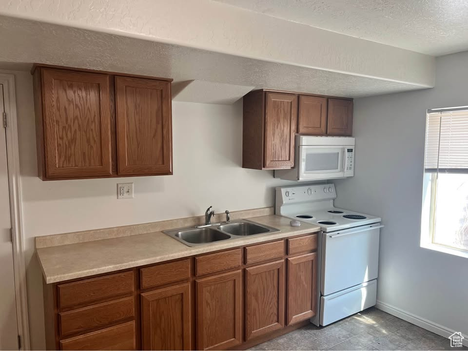 Kitchen featuring white appliances, light countertops, brown cabinets, and a textured ceiling