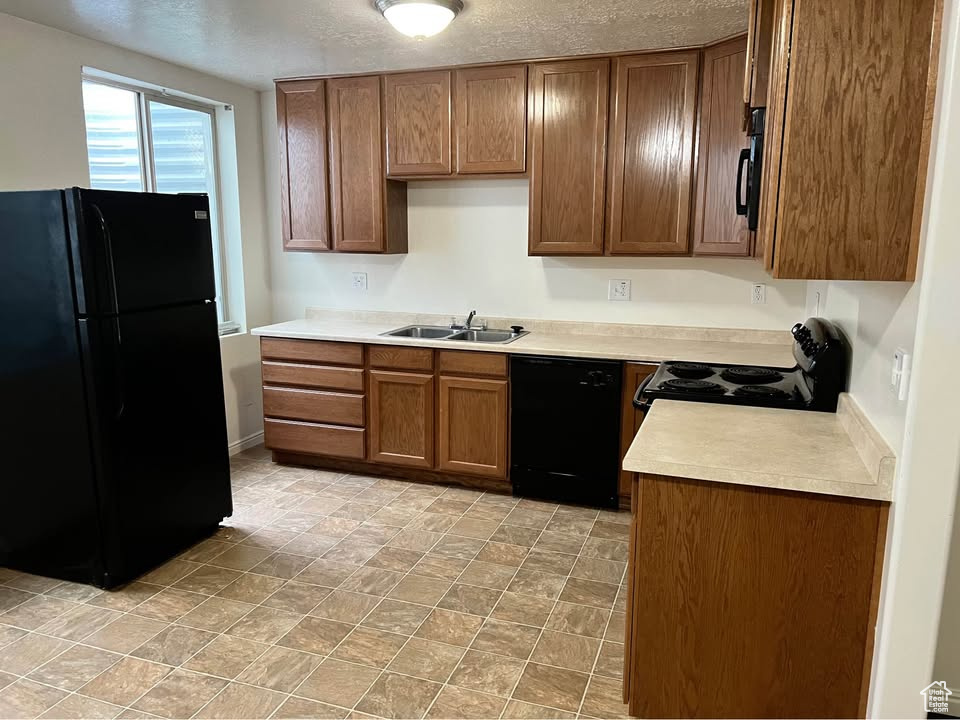 Kitchen with black appliances, a textured ceiling, brown cabinets, and light countertops