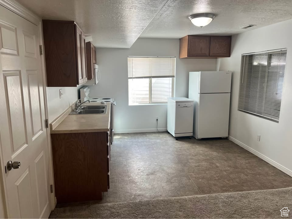 Kitchen with freestanding refrigerator, a textured ceiling, fridge, light countertops, and dark brown cabinets