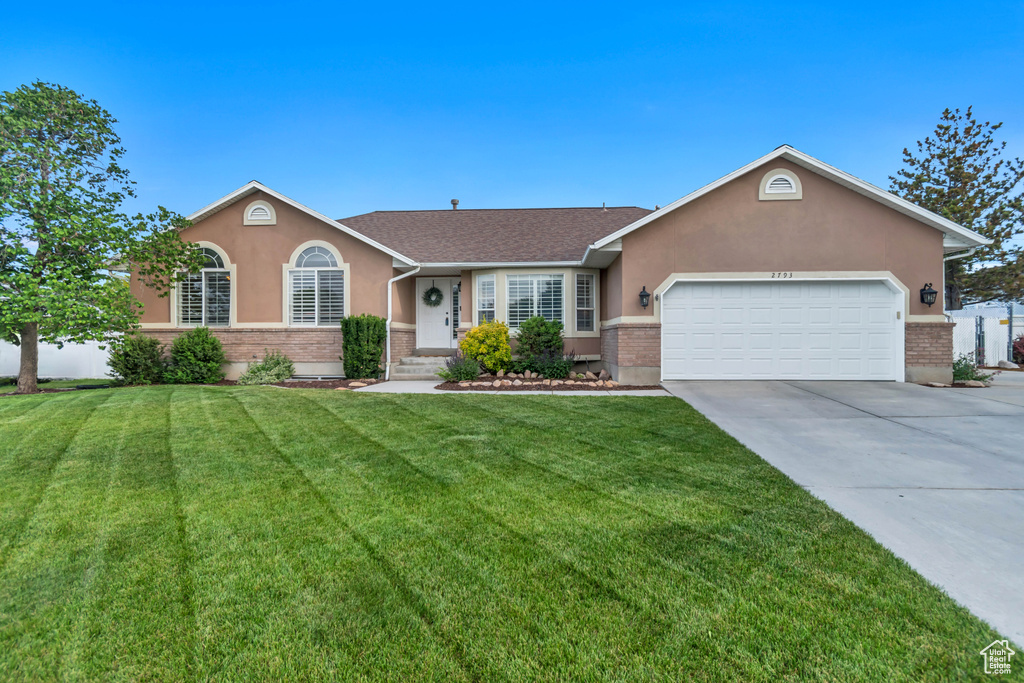 Single story home with brick siding, an attached garage, driveway, and a front lawn
