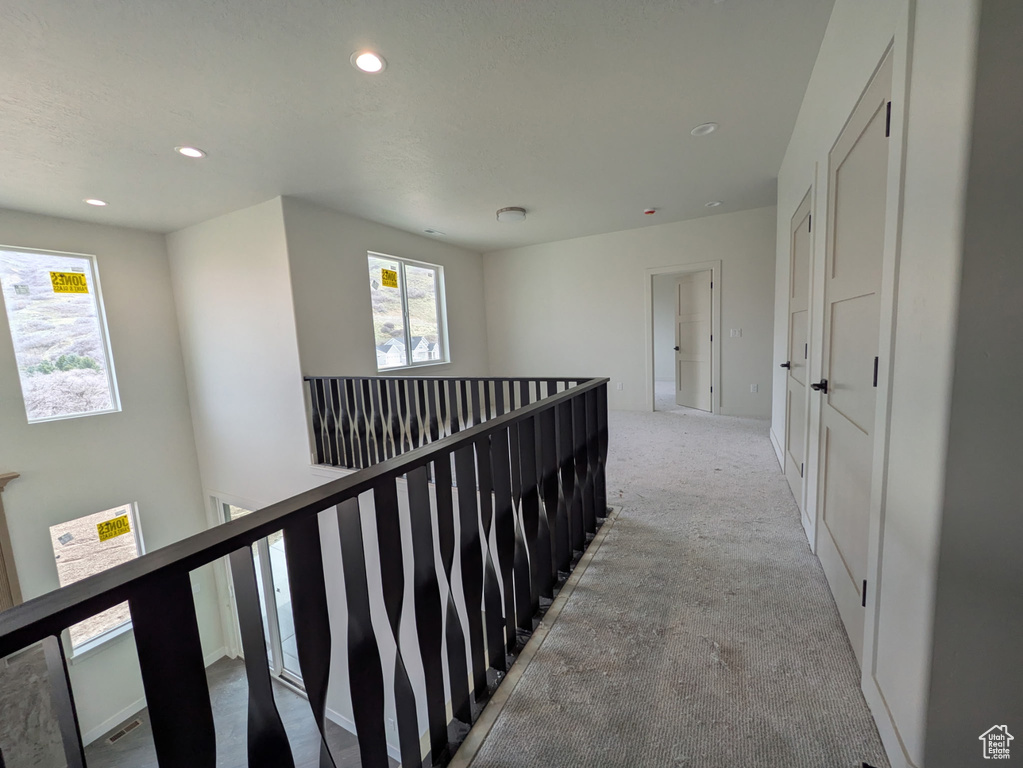 Hall with plenty of natural light, light carpet, an upstairs landing, and recessed lighting