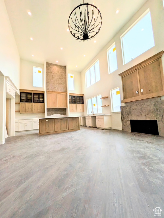 Unfurnished living room featuring a high ceiling, a fireplace, light wood-type flooring, and a notable chandelier