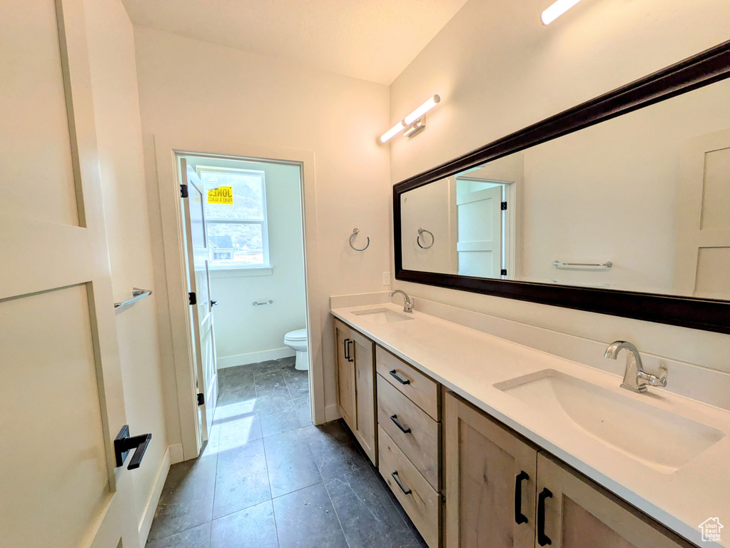 Bathroom with baseboards, double vanity, a sink, and toilet