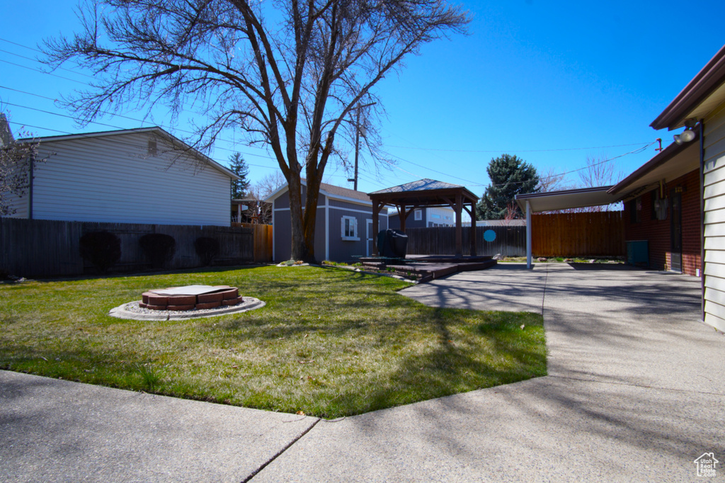 View of yard with an outdoor structure, a fenced backyard, an outdoor fire pit, a gazebo, and a carport
