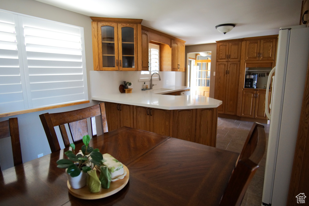 Kitchen with a sink, freestanding refrigerator, a peninsula, brown cabinets, and glass insert cabinets