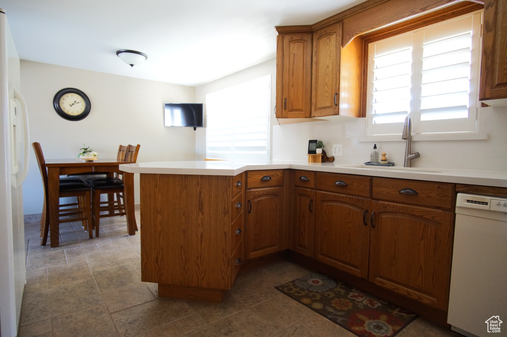 Kitchen featuring light countertops, a sink, a peninsula, brown cabinetry, and white appliances