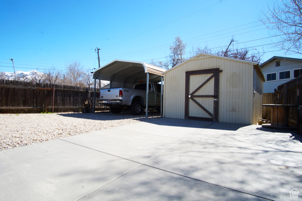 View of shed with fence, concrete driveway, and a carport