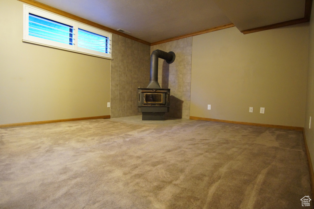 Unfurnished living room with baseboards, visible vents, a wood stove, and carpet flooring