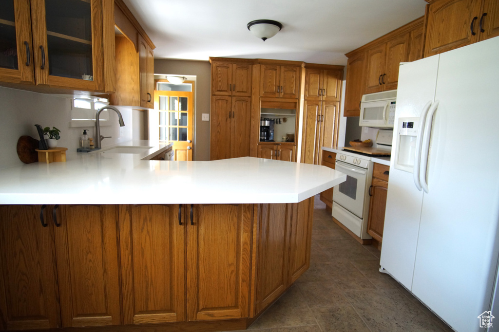 Kitchen featuring light countertops, white appliances, a sink, a peninsula, and glass insert cabinets