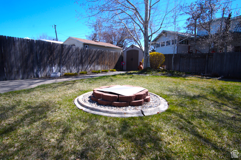 View of yard with a fenced backyard, a fire pit, a storage unit, and an outdoor structure