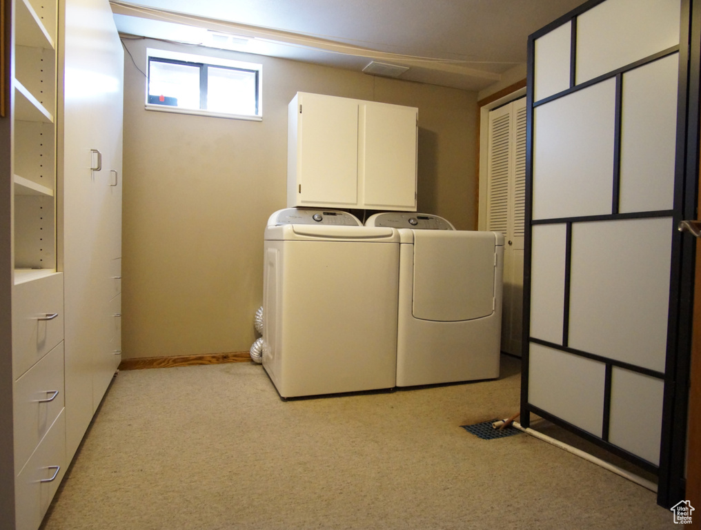 Clothes washing area featuring washing machine and clothes dryer, cabinet space, and light carpet
