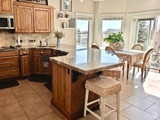 Kitchen featuring a breakfast bar area, a sink, light tile patterned floors, stainless steel microwave, and a peninsula