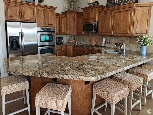 Kitchen with brown cabinets, a sink, stainless steel appliances, a peninsula, and decorative backsplash