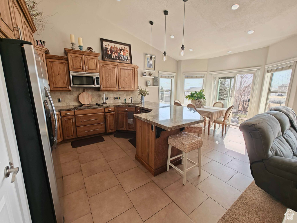 Kitchen featuring brown cabinetry, a kitchen bar, a peninsula, open floor plan, and stainless steel appliances