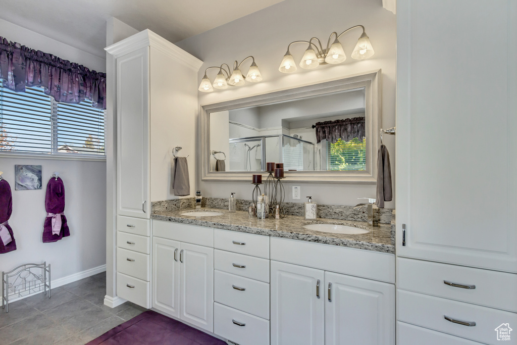 Bathroom featuring tile patterned flooring, baseboards, a shower stall, a sink, and double vanity