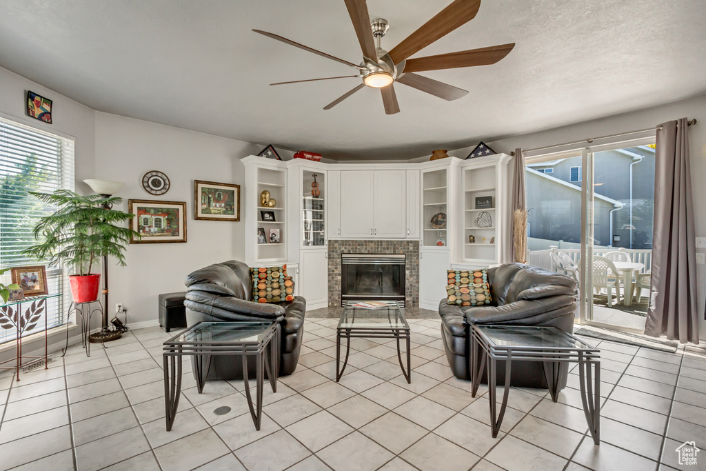 Living room featuring a fireplace, a textured ceiling, light tile patterned floors, baseboards, and ceiling fan