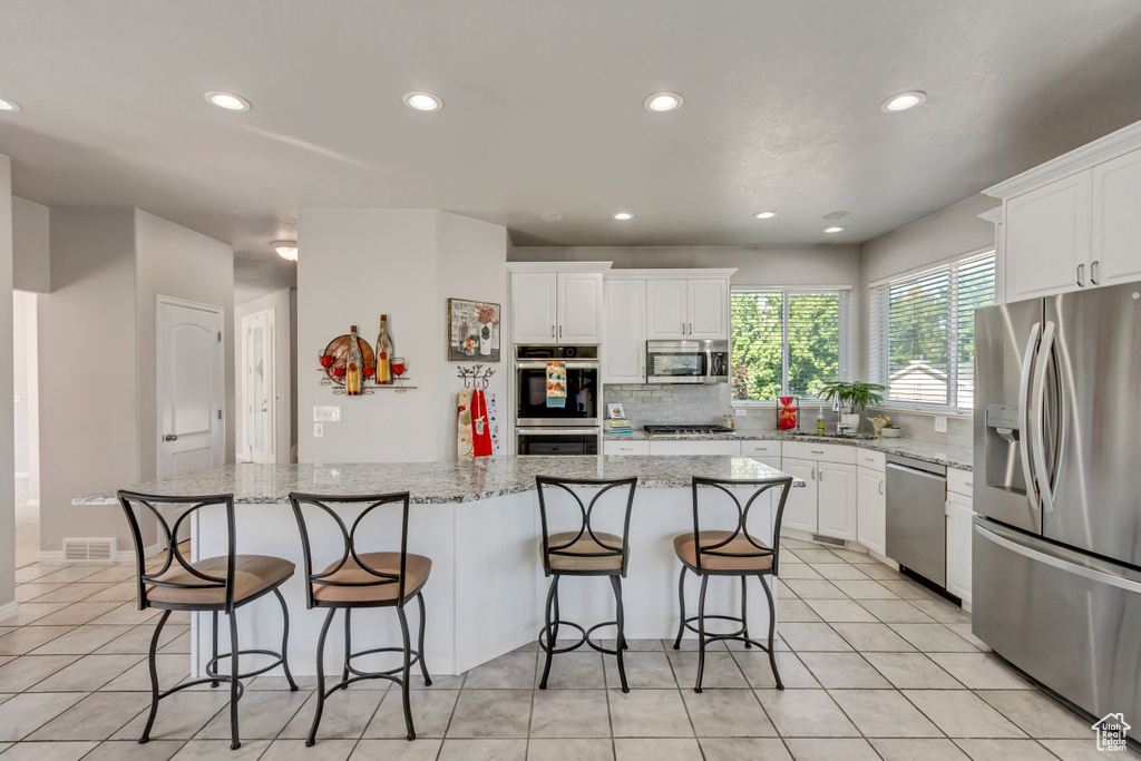 Kitchen with backsplash, a kitchen bar, appliances with stainless steel finishes, light tile patterned floors, and white cabinets