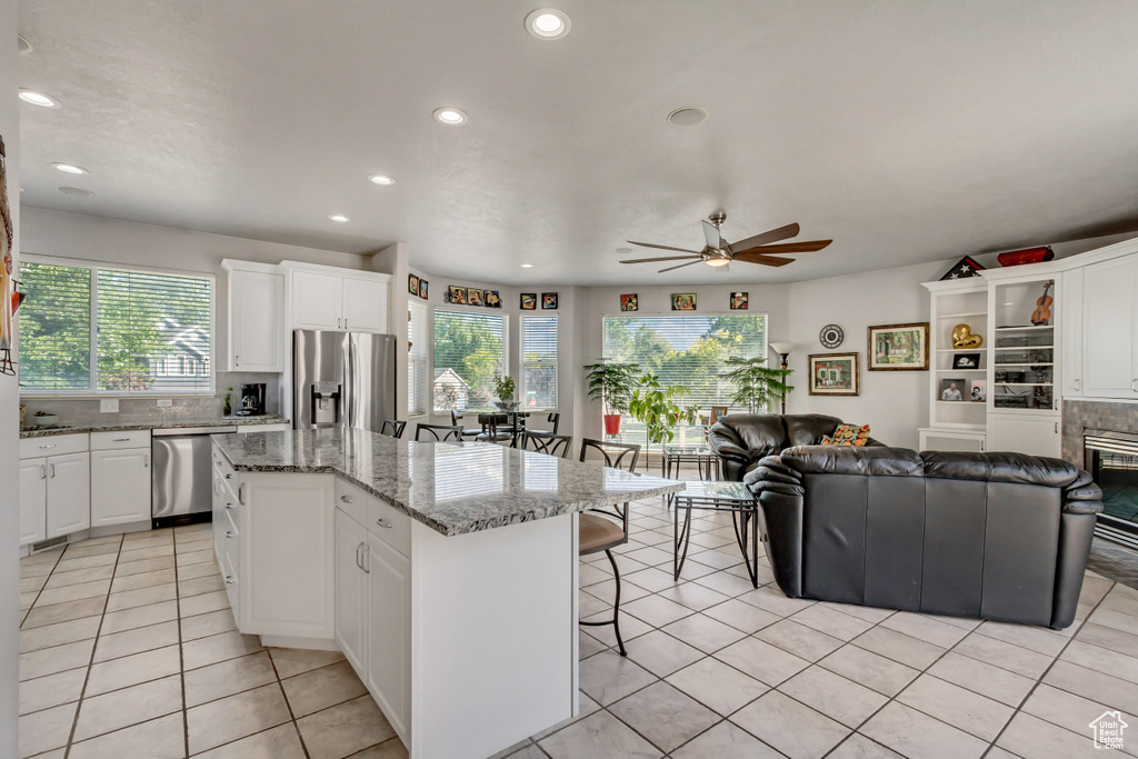 Kitchen with light tile patterned floors, a kitchen island, ceiling fan, white cabinets, and appliances with stainless steel finishes