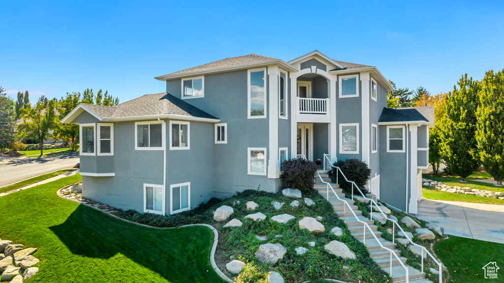 View of front facade with a balcony, a front yard, and stucco siding