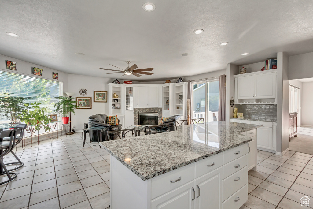 Kitchen featuring decorative backsplash, a kitchen island, a ceiling fan, a glass covered fireplace, and light tile patterned floors