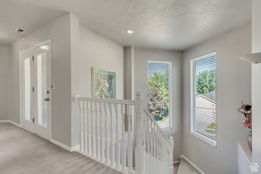 Hall with a textured ceiling, an upstairs landing, visible vents, carpet, and baseboards