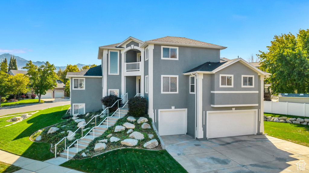 View of front of home featuring a front yard, concrete driveway, stucco siding, a balcony, and a garage