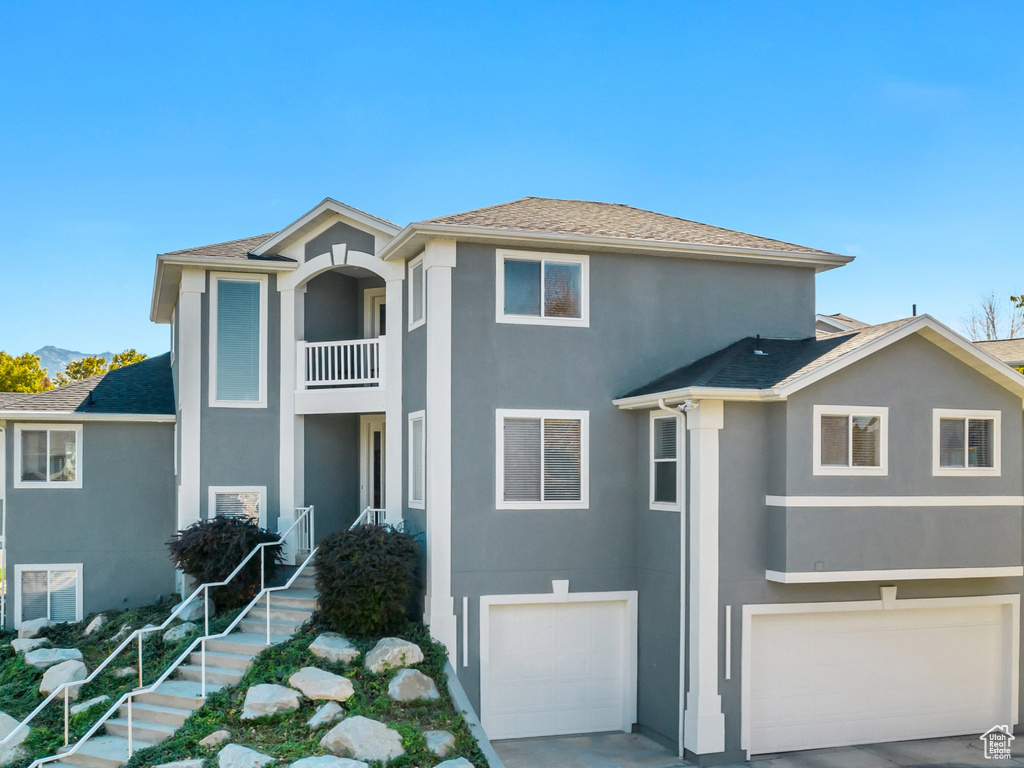 View of front of home featuring a front yard, concrete driveway, stucco siding, a balcony, and a garage