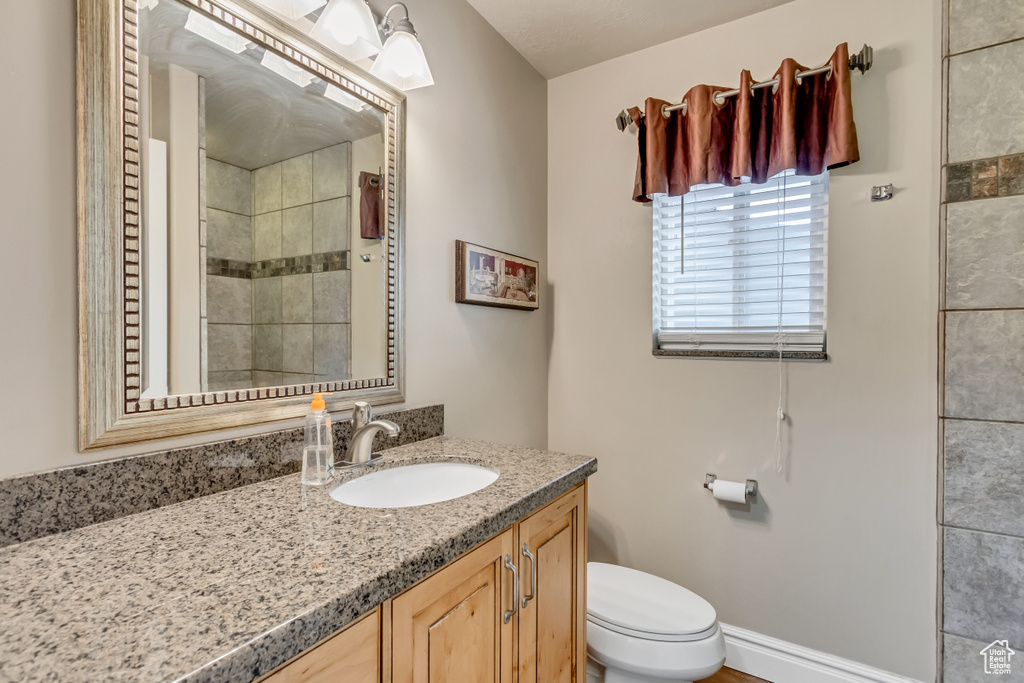 Full bathroom featuring baseboards, toilet, a tile shower, and vanity