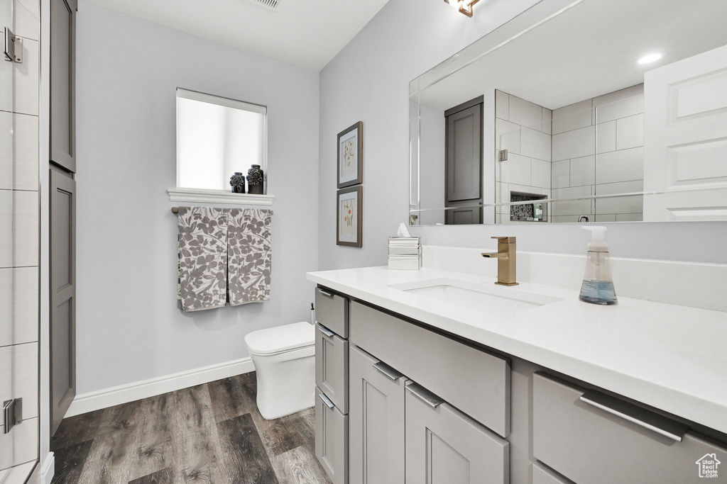 Bathroom with baseboards, toilet, wood finished floors, vanity, and tiled shower