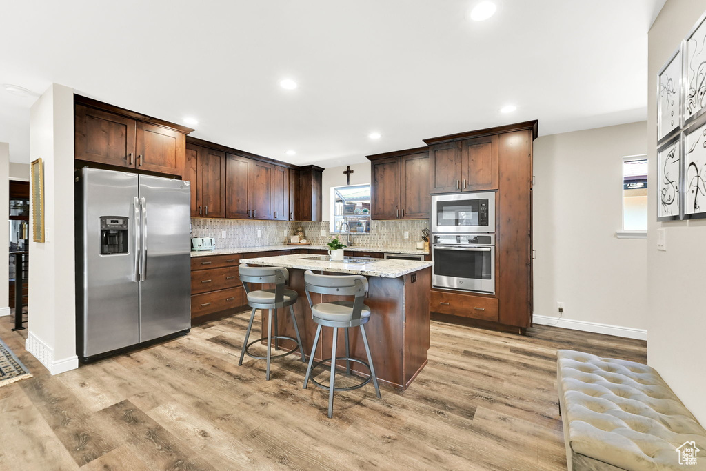 Kitchen featuring a breakfast bar area, a center island, backsplash, light wood finished floors, and appliances with stainless steel finishes