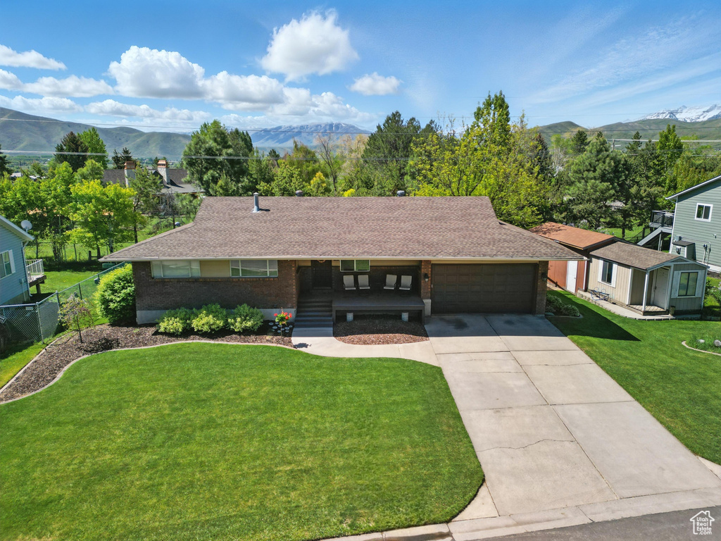 Ranch-style house featuring an attached garage, concrete driveway, brick siding, a mountain view, and a shingled roof