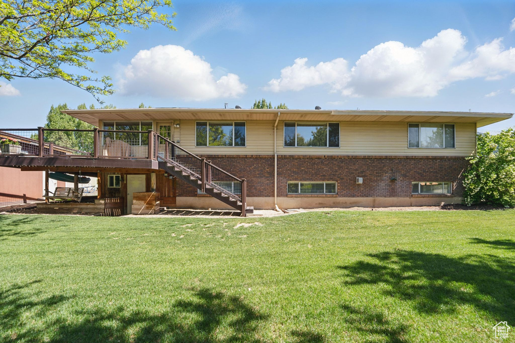 Back of property with stairway, a wooden deck, brick siding, and a yard