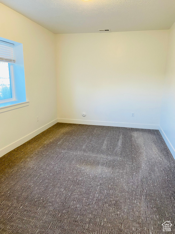 Empty room featuring dark colored carpet, baseboards, and visible vents