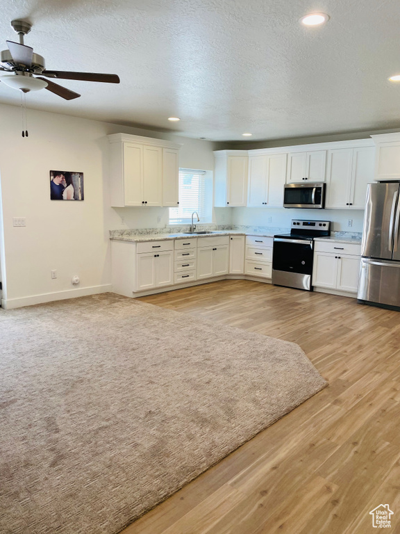 Kitchen with a sink, light wood finished floors, white cabinetry, a ceiling fan, and appliances with stainless steel finishes