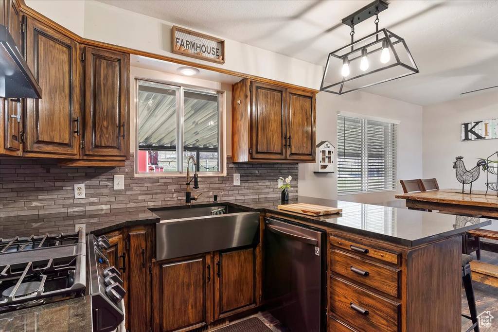 Kitchen with under cabinet range hood, stainless steel dishwasher, backsplash, a sink, and a peninsula
