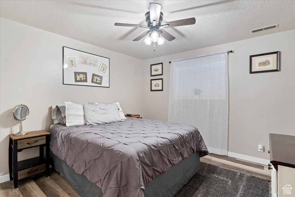 Bedroom featuring a textured ceiling, visible vents, baseboards, ceiling fan, and wood finished floors