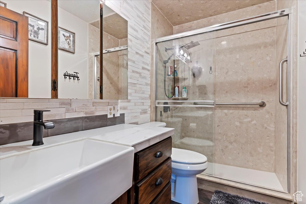 Bathroom with a stall shower, toilet, vanity, and backsplash