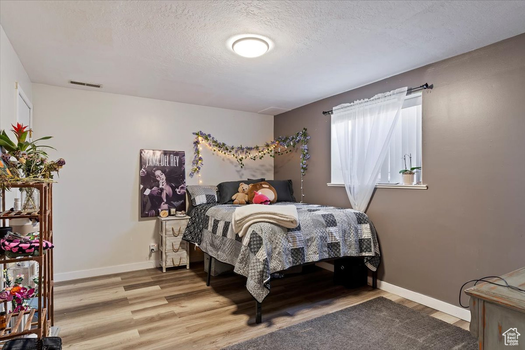 Bedroom with light wood-style flooring, visible vents, baseboards, and a textured ceiling