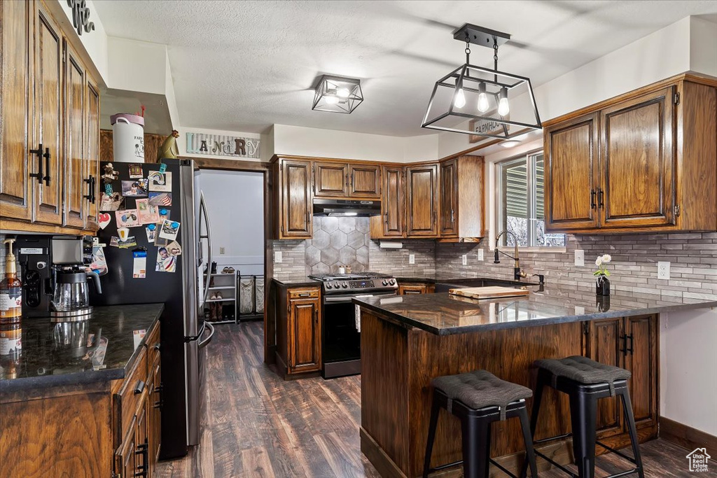 Kitchen featuring tasteful backsplash, appliances with stainless steel finishes, a peninsula, dark wood finished floors, and under cabinet range hood