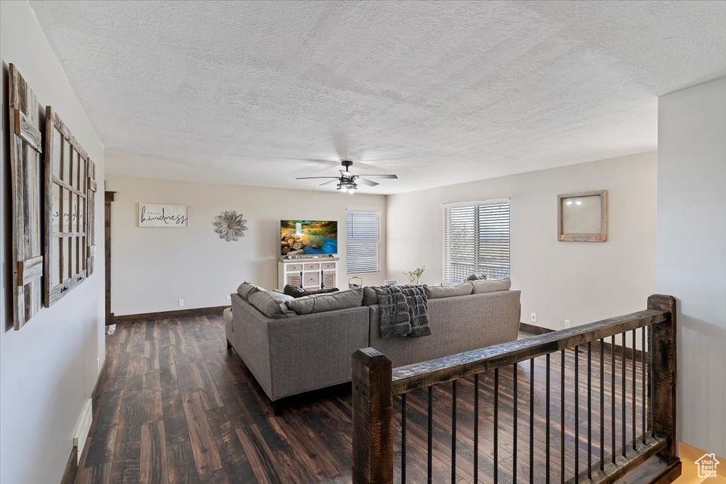 Living room with a ceiling fan, a textured ceiling, baseboards, and wood finished floors