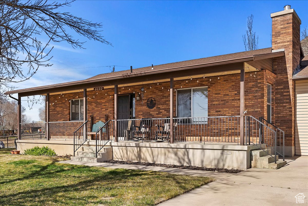 Single story home featuring brick siding, a chimney, a porch, and a front yard